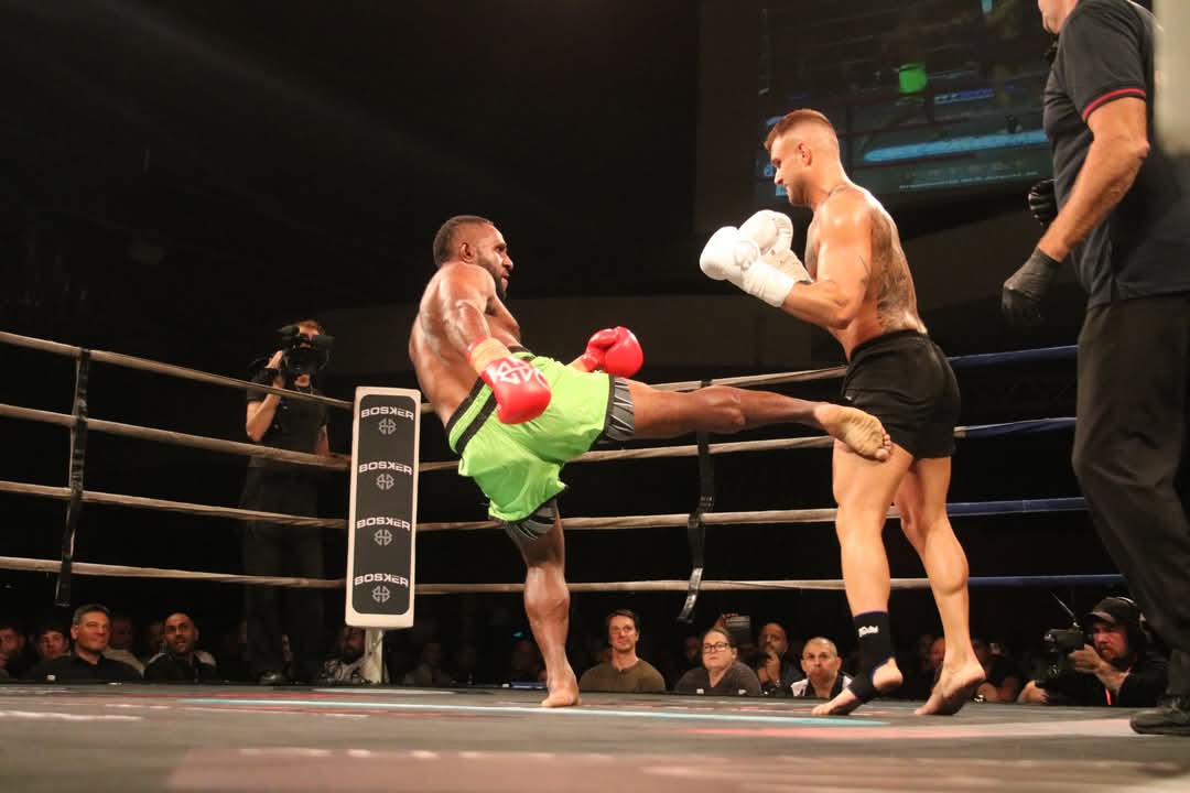 PNG kickboxer in green shorts landing a high kick on his opponent