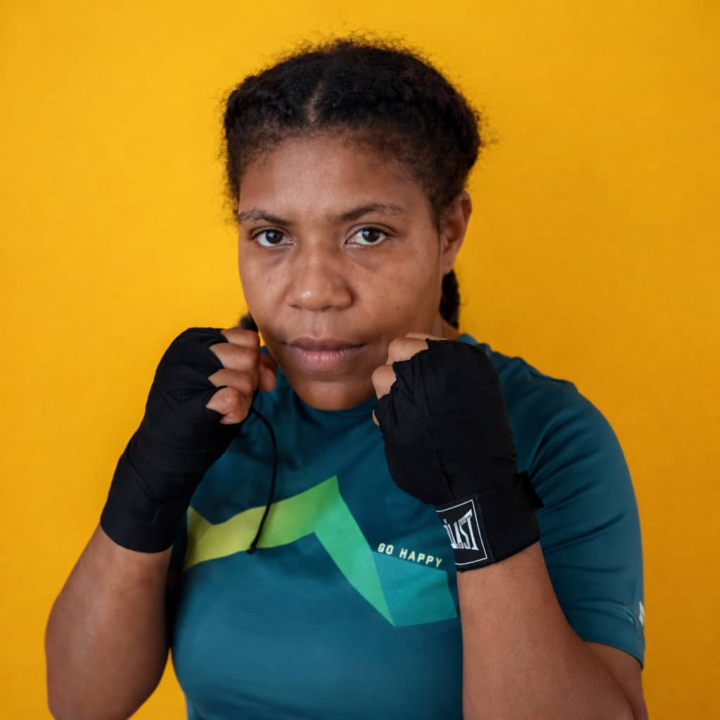 Female PNG boxer with hand wraps in guard against a yellow backdrop