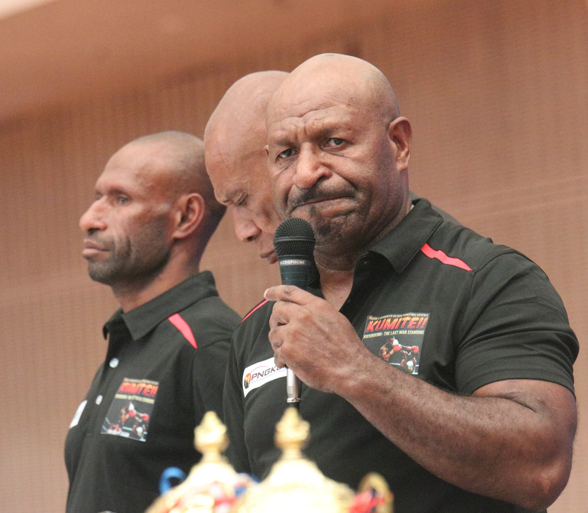 PNGKBF officials in Headhunter KO polos addressing the crowd beside championship trophies