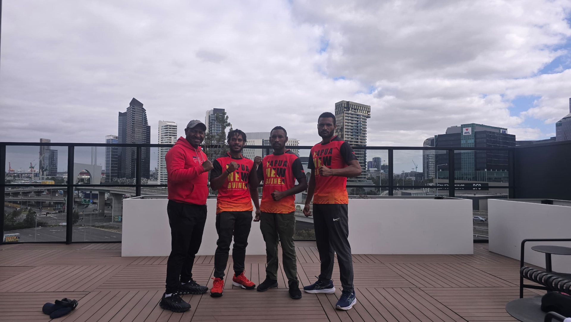 PNG team in national jerseys posing on a rooftop with the Melbourne skyline behind them