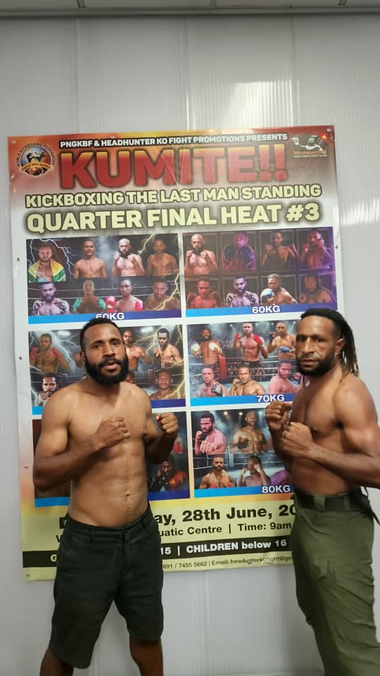 Two PNG kickboxers posing together in front of the KUMITE tournament poster