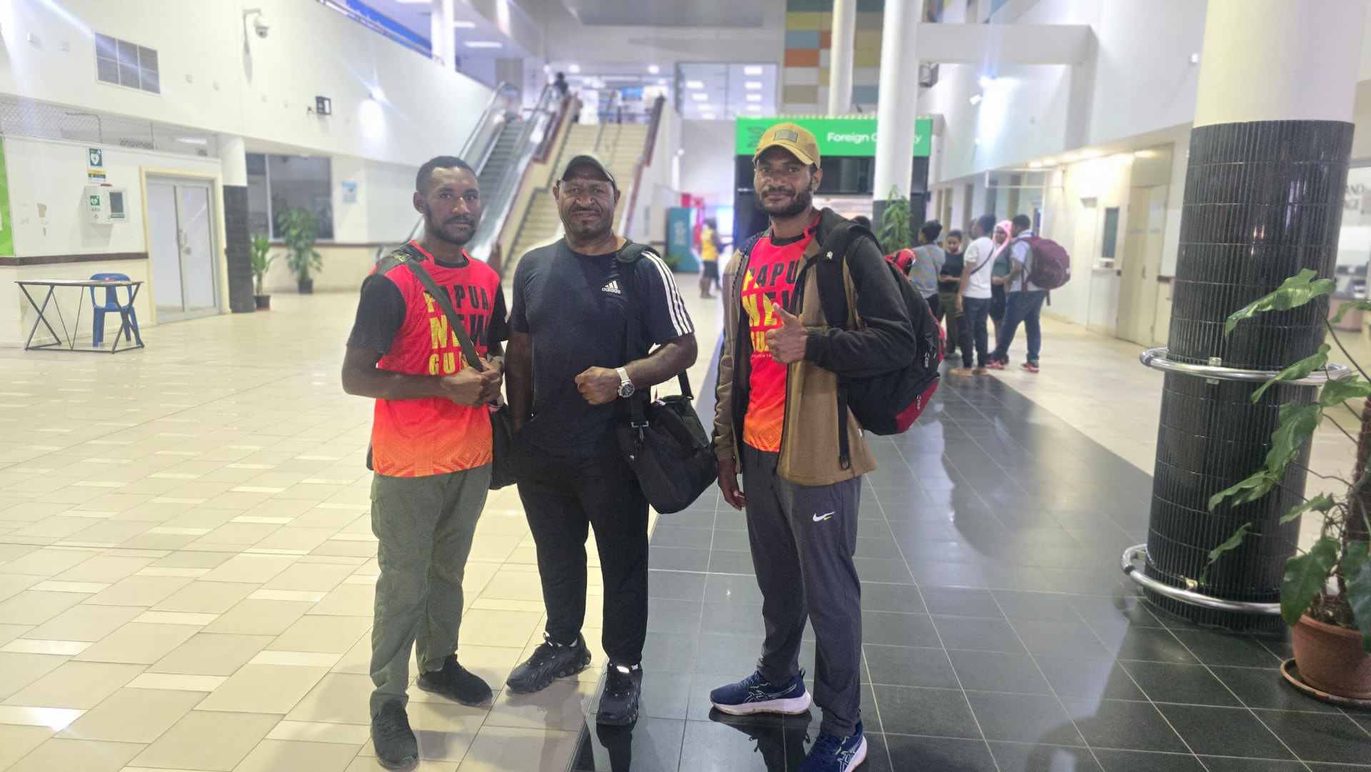 PNG kickboxers and their coach posing at the airport in Papua New Guinea jerseys