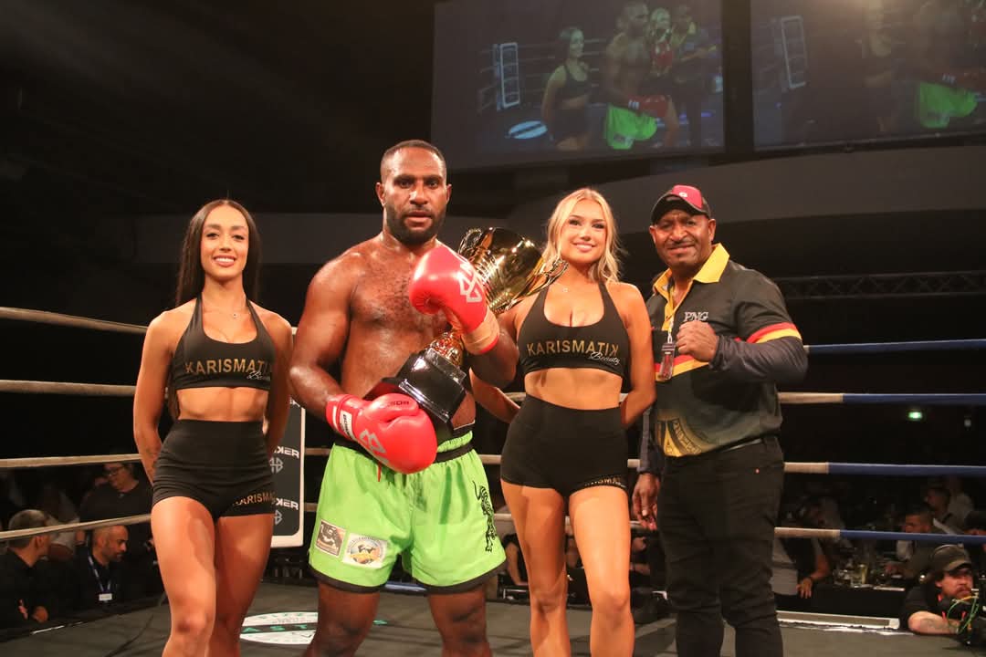 PNG kickboxer holding a gold championship trophy in the ring with ring girls and a PNG official